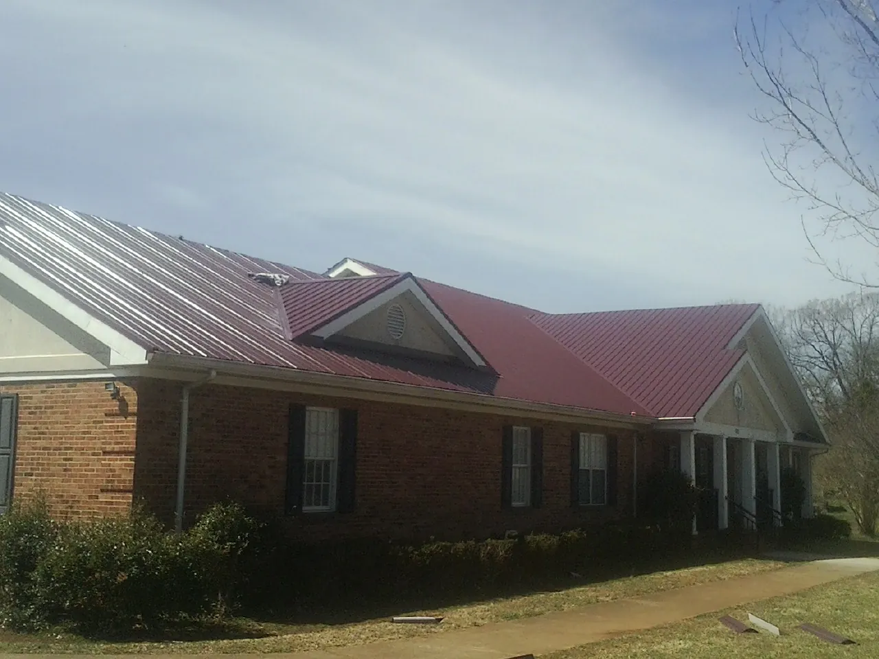 Red metal roof with gabled entries on a long brick building, from a Hail Damage Roof Repair job in Cumberland Gap