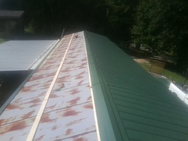 Old rusted panels beside newly installed green metal roofing — Wind Damage Roof Repair by Roofing Brothers in Cumberland Gap