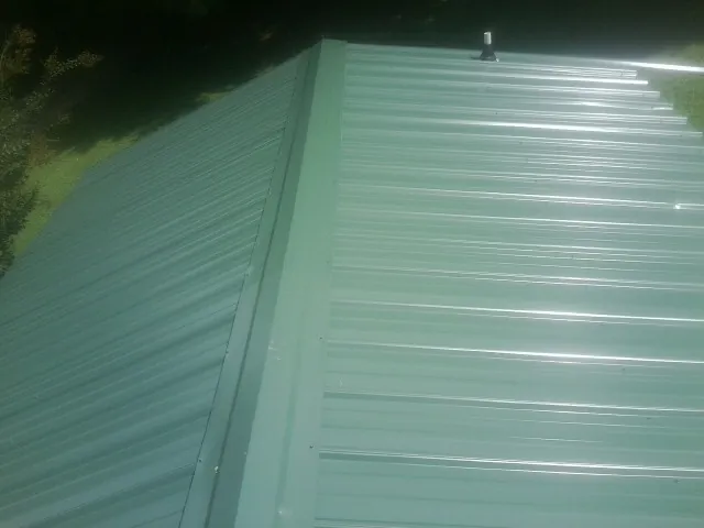 New green metal panels meeting at the ridge of a roof — Flat Roof Repair work by our crew in Cumberland Gap