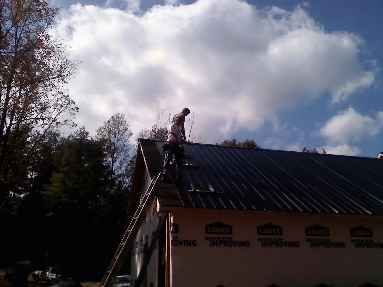 Roofer fastening dark metal panels high against a cloudy sky, from a Roof Inspection job in Cumberland Gap