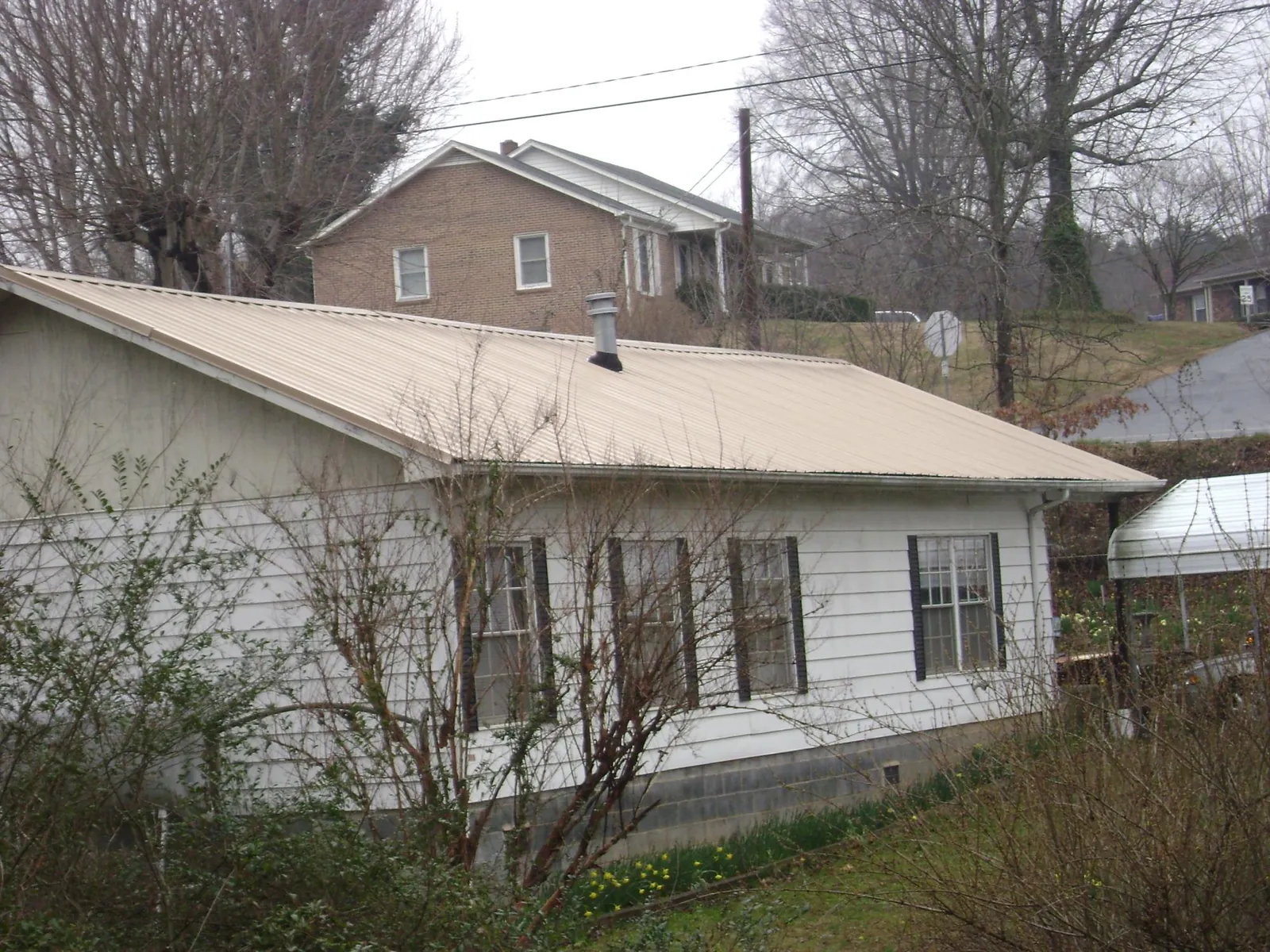 Tan metal roof on a white sided house set into a hillside — Commercial Roofing by Roofing Brothers in Cumberland Gap