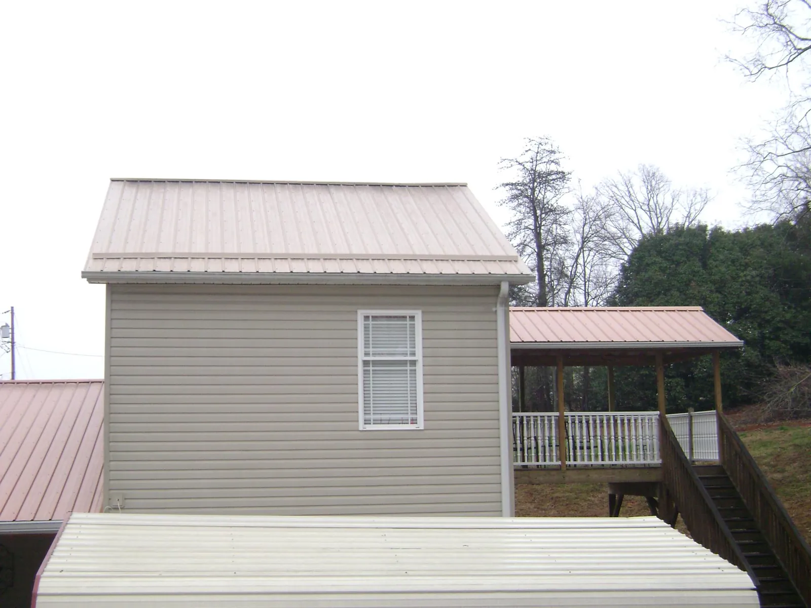 Tan metal roofs on a two story addition and attached porch, from a Roof Replacement job in Cumberland Gap