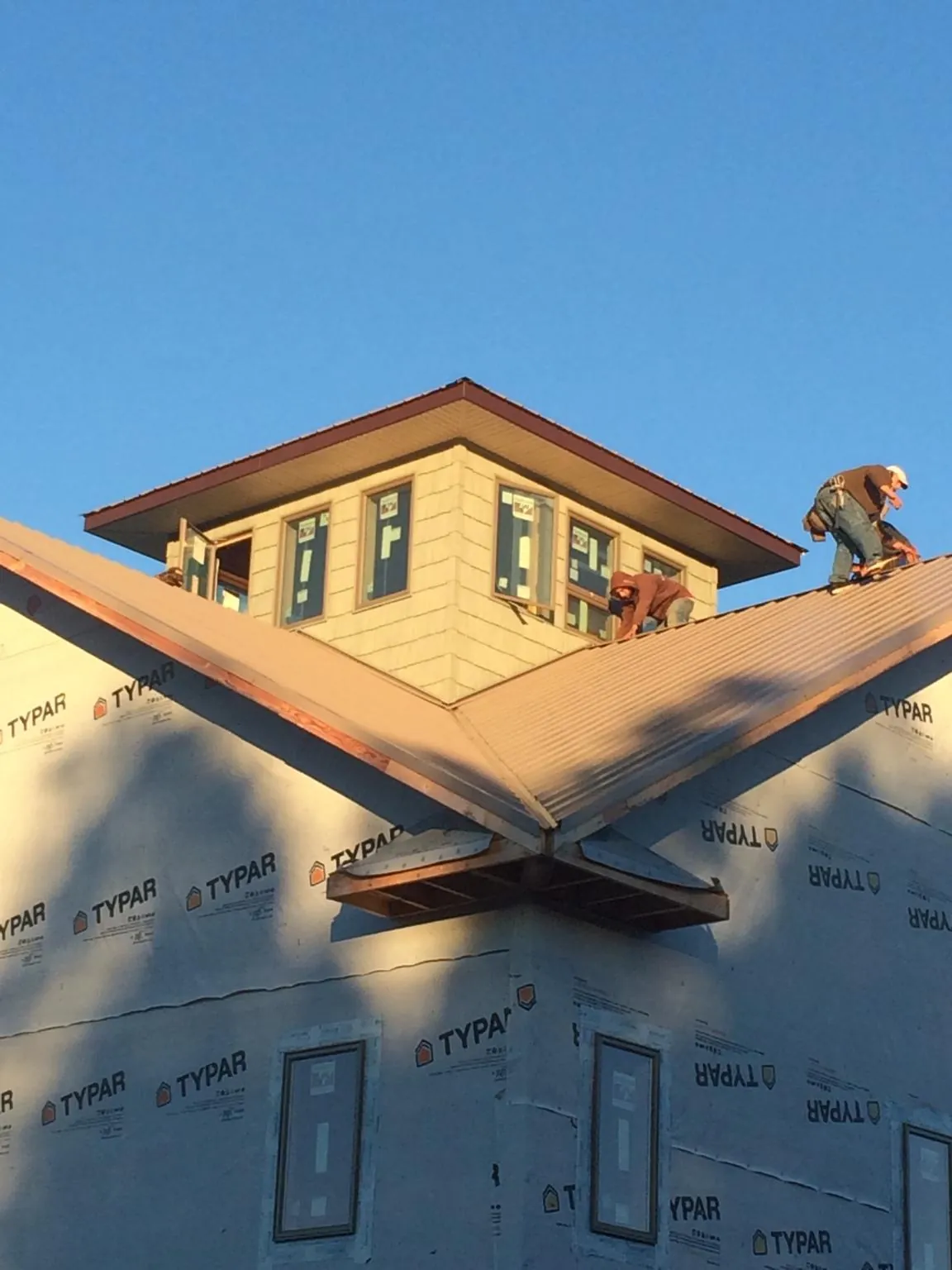 Roofers working around a rooftop cupola on a new metal roof at sunset — Roof Waterproofing in Cumberland Gap by Roofing Brothers